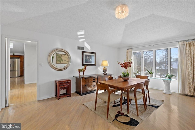 dining area with a notable chandelier, a textured ceiling, and light wood-type flooring