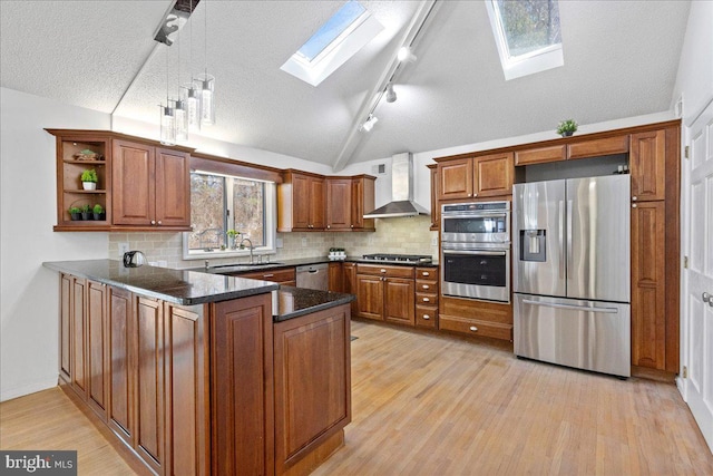 kitchen featuring lofted ceiling with skylight, appliances with stainless steel finishes, kitchen peninsula, decorative backsplash, and wall chimney range hood