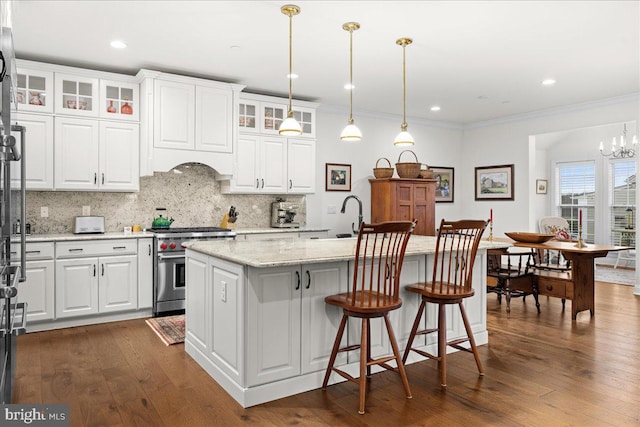 kitchen with pendant lighting, white cabinetry, light stone counters, high end stainless steel range oven, and a kitchen island with sink