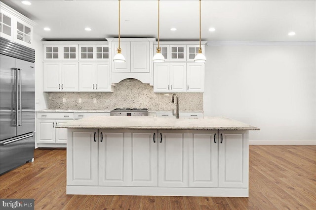 kitchen featuring pendant lighting, an island with sink, white cabinetry, built in refrigerator, and light stone counters