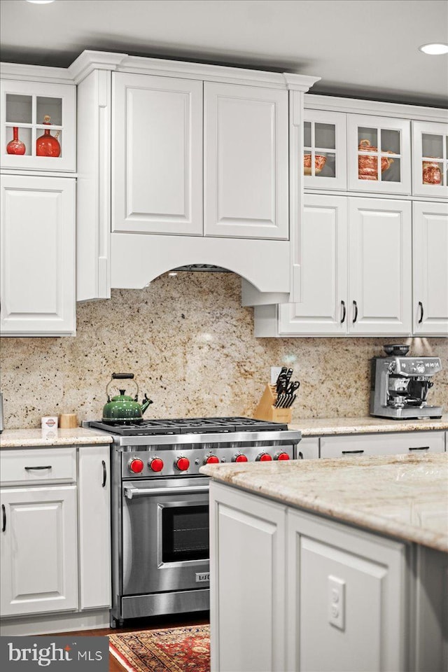 kitchen featuring white cabinetry, premium stove, light stone countertops, and decorative backsplash