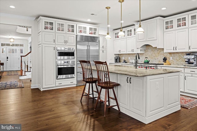 kitchen with pendant lighting, white cabinetry, stainless steel appliances, light stone countertops, and a center island with sink