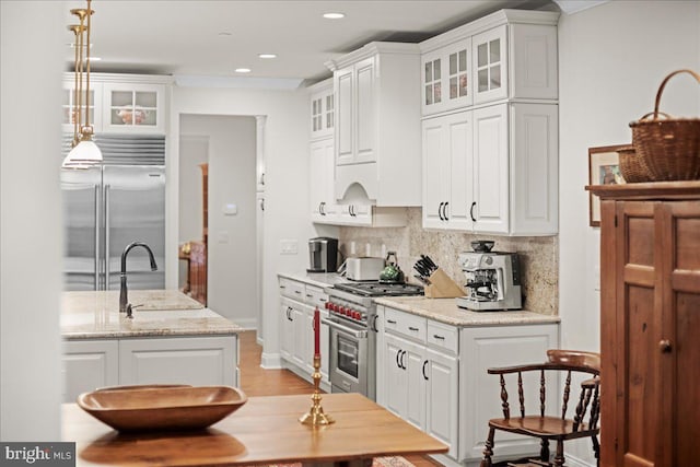 kitchen featuring pendant lighting, high quality appliances, white cabinetry, sink, and light stone counters