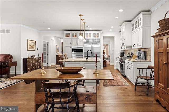 kitchen with high end appliances, light stone counters, white cabinets, a center island with sink, and decorative light fixtures