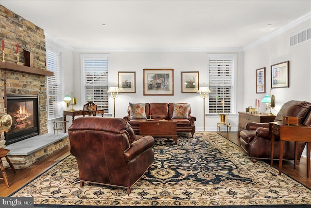 living room with wood-type flooring, a stone fireplace, and crown molding