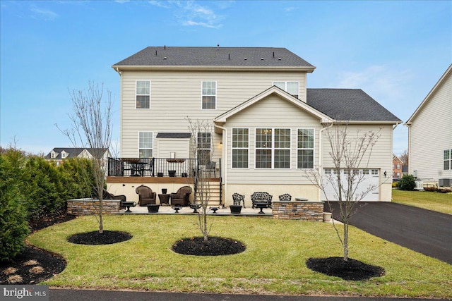 back of property featuring a garage, a lawn, and a deck