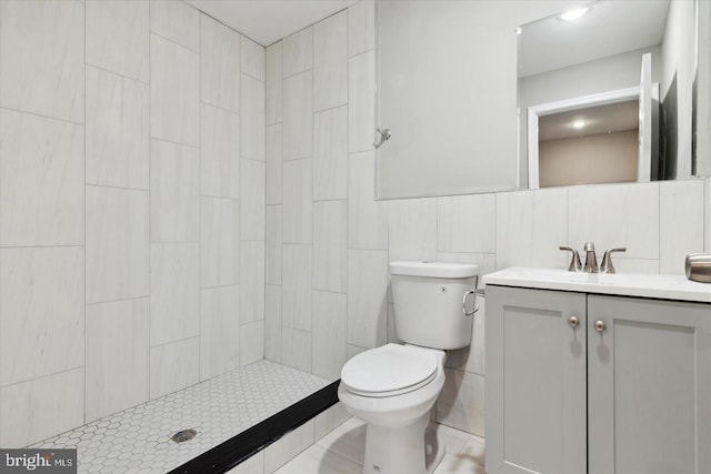 bathroom featuring a tile shower, vanity, tile walls, and toilet