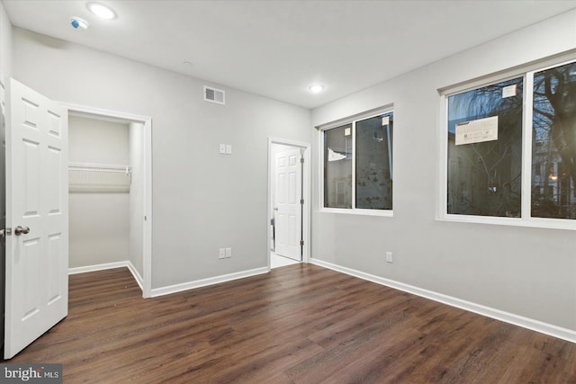 unfurnished bedroom with a closet, a spacious closet, and dark hardwood / wood-style flooring