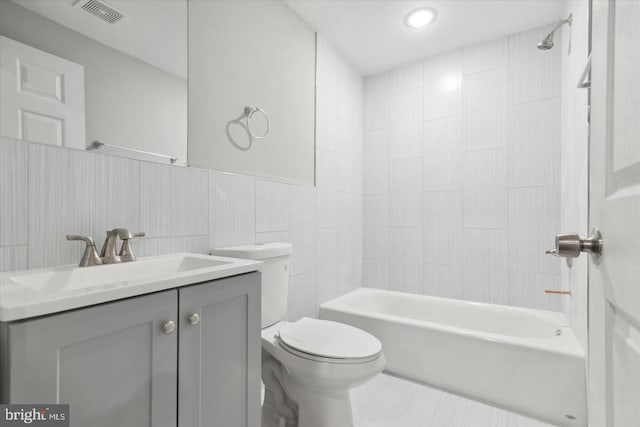 full bathroom featuring vanity, toilet, tile walls, and tiled shower / bath