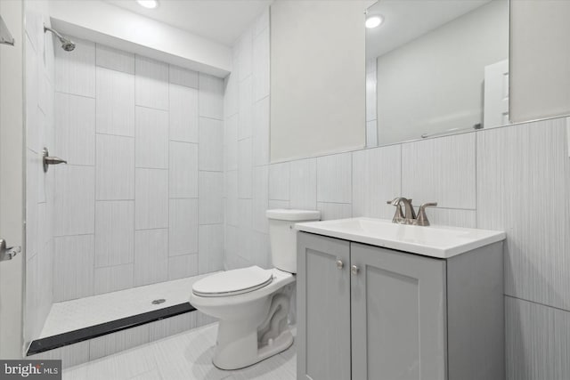 bathroom featuring a tile shower, vanity, tile walls, and toilet