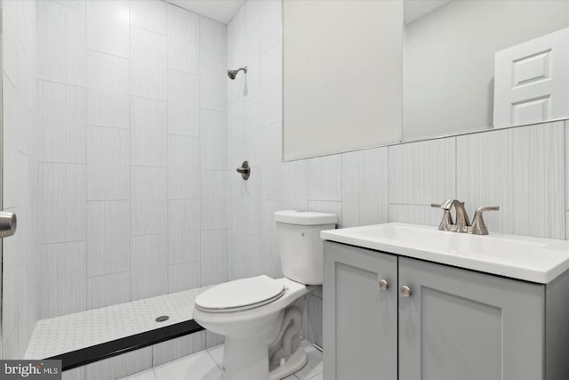 bathroom with tiled shower, vanity, toilet, and tile walls