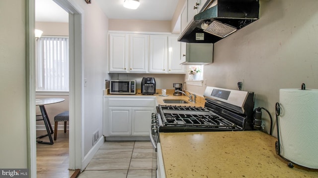 kitchen with stainless steel appliances, sink, white cabinetry, light tile patterned flooring, and ventilation hood