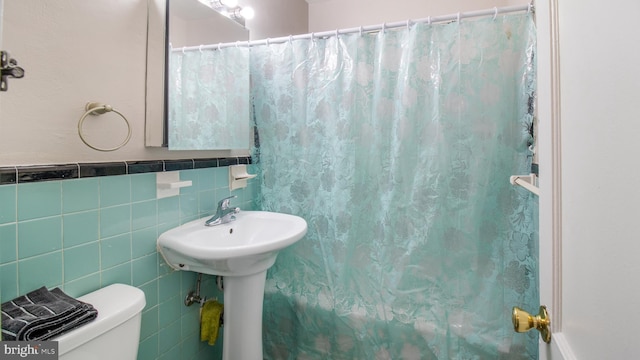 bathroom with toilet, a shower with shower curtain, tile walls, and sink