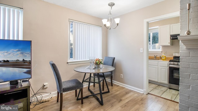 dining space with sink, a fireplace, a notable chandelier, and light hardwood / wood-style flooring