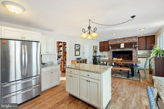 kitchen with stainless steel fridge, a brick fireplace, decorative light fixtures, a chandelier, and white cabinets