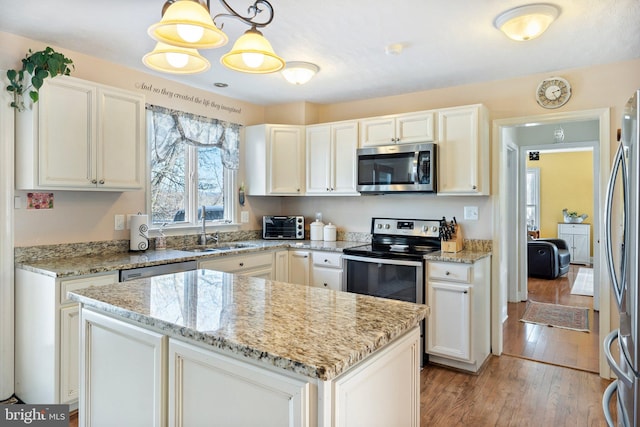 kitchen with pendant lighting, a kitchen island, white cabinetry, stainless steel appliances, and sink