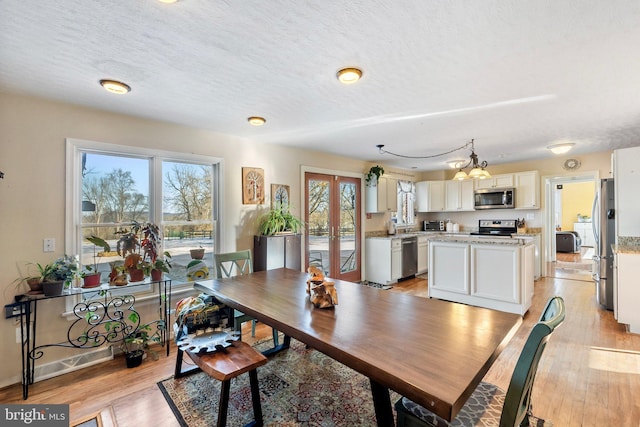 dining area with light wood-type flooring, french doors, a chandelier, and a textured ceiling