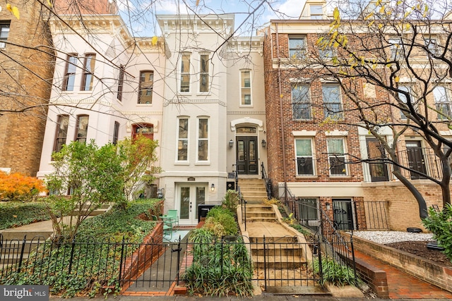 view of property with a fenced front yard, french doors, and brick siding