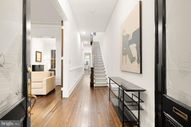 foyer entrance with crown molding, wood-type flooring, a decorative wall, stairway, and wainscoting