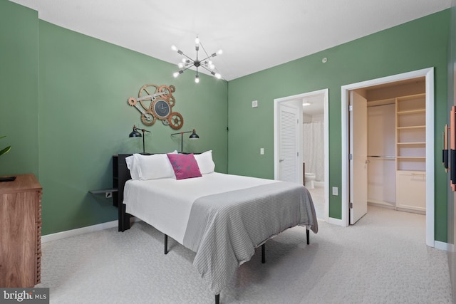 carpeted bedroom with a walk in closet, ensuite bathroom, and an inviting chandelier