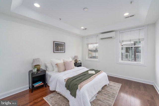 bedroom with baseboards, a raised ceiling, dark wood finished floors, a wall unit AC, and recessed lighting