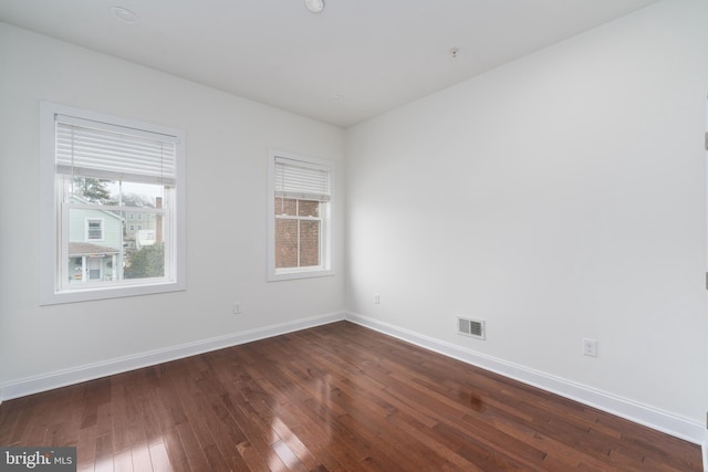 unfurnished room with baseboards, visible vents, and dark wood-style flooring