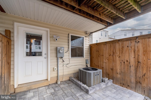 view of exterior entry with a patio area, cooling unit, and fence