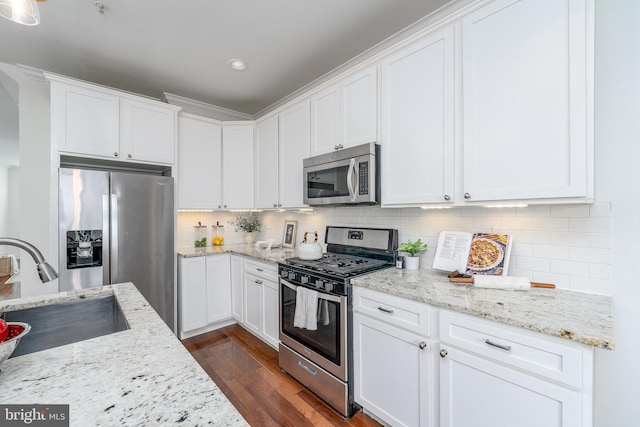 kitchen featuring tasteful backsplash, light stone countertops, stainless steel appliances, white cabinetry, and a sink