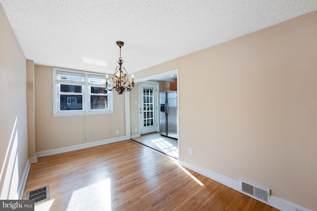 unfurnished dining area with light hardwood / wood-style floors, a textured ceiling, and an inviting chandelier