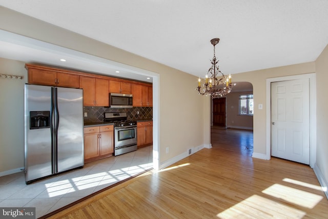 kitchen featuring hanging light fixtures, stainless steel appliances, light hardwood / wood-style flooring, a notable chandelier, and backsplash