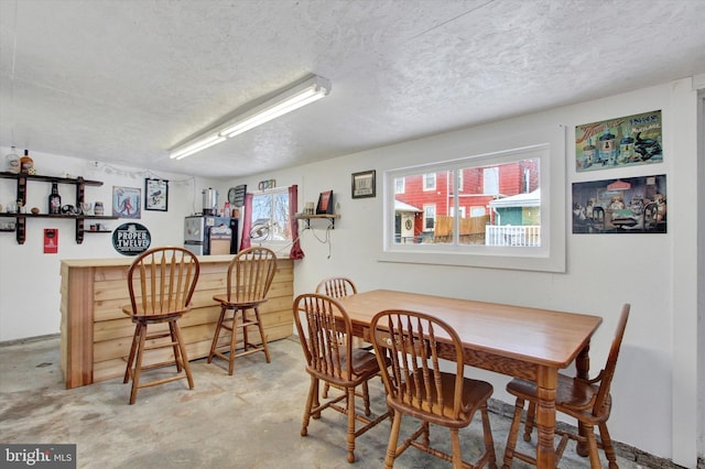 dining space with plenty of natural light, concrete flooring, a textured ceiling, and bar area