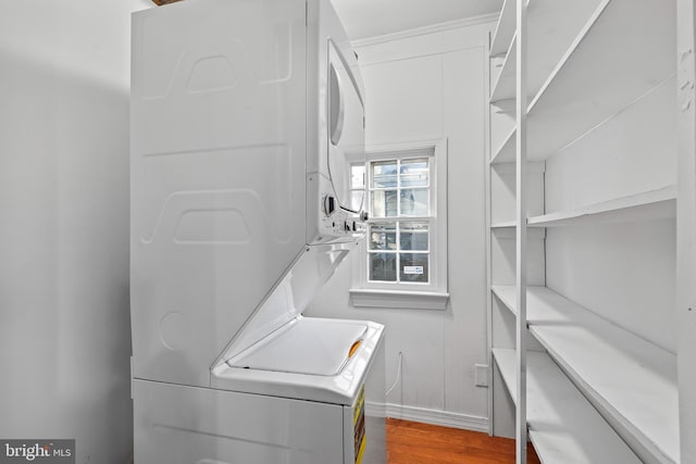 laundry room featuring stacked washer and dryer, wood finished floors, laundry area, and baseboards