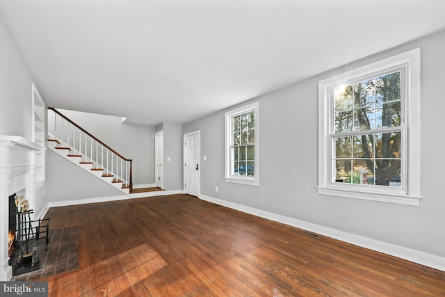 foyer entrance with visible vents, dark wood-type flooring, a fireplace with flush hearth, baseboards, and stairs