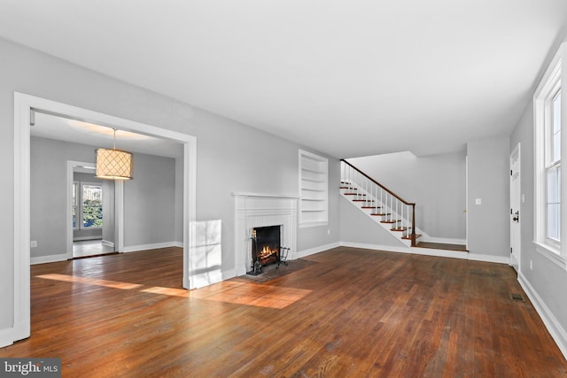 unfurnished living room featuring visible vents, stairway, dark wood-type flooring, a fireplace with flush hearth, and baseboards