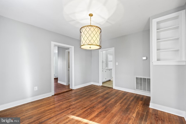 unfurnished dining area featuring dark wood-style floors, baseboards, visible vents, and built in features