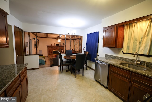 kitchen with a fireplace, stainless steel dishwasher, sink, pendant lighting, and dark stone counters