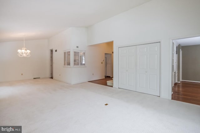 spare room with carpet floors, high vaulted ceiling, and an inviting chandelier