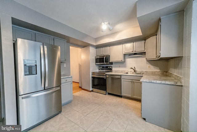 kitchen with sink, decorative backsplash, gray cabinets, light tile patterned floors, and appliances with stainless steel finishes