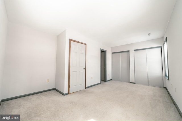 unfurnished bedroom with light colored carpet and multiple closets