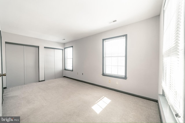 unfurnished bedroom featuring light colored carpet and multiple closets