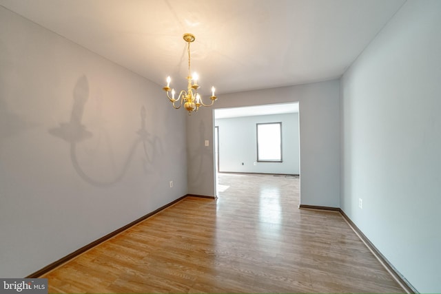 empty room featuring light wood-type flooring and a notable chandelier