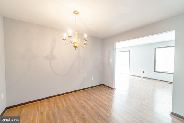 empty room with wood-type flooring and an inviting chandelier