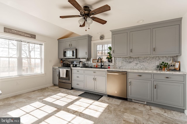 kitchen with appliances with stainless steel finishes, backsplash, gray cabinetry, ceiling fan, and lofted ceiling