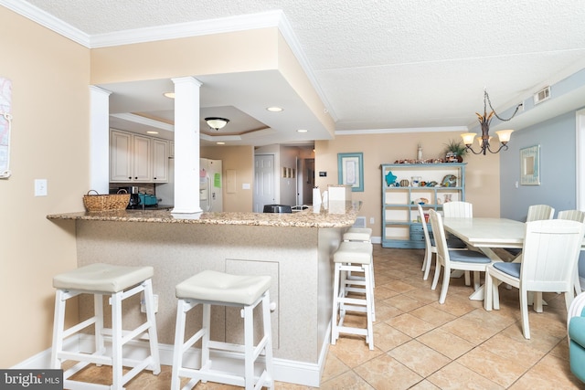 kitchen featuring kitchen peninsula, crown molding, decorative light fixtures, a notable chandelier, and a breakfast bar area