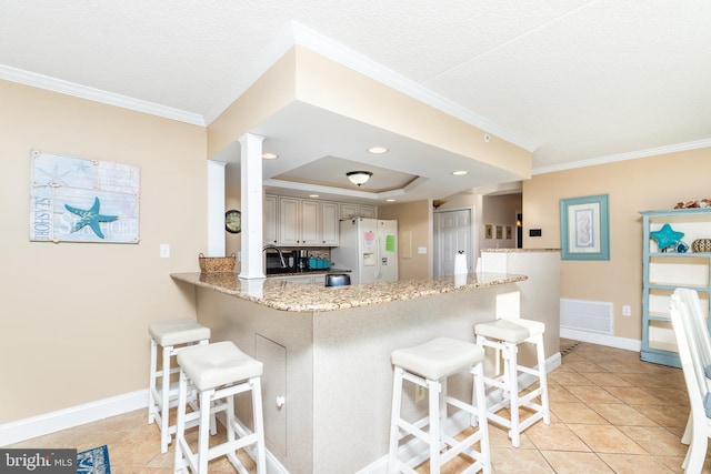 kitchen with a kitchen breakfast bar, a tray ceiling, light tile patterned flooring, and white refrigerator with ice dispenser