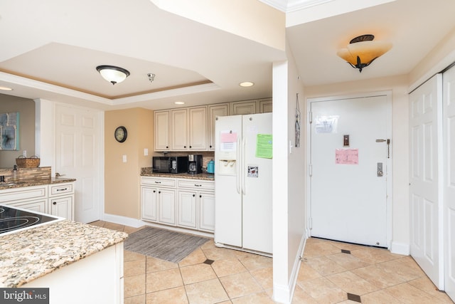 kitchen featuring a tray ceiling, light stone countertops, white fridge with ice dispenser, and light tile patterned floors