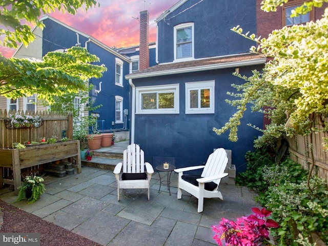 back of house at dusk featuring a patio, fence, and stucco siding