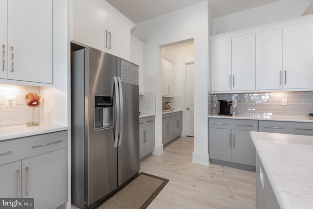 kitchen featuring backsplash, stainless steel fridge with ice dispenser, and light stone counters