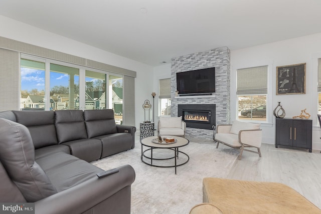 living room with light hardwood / wood-style floors, a stone fireplace, and a healthy amount of sunlight