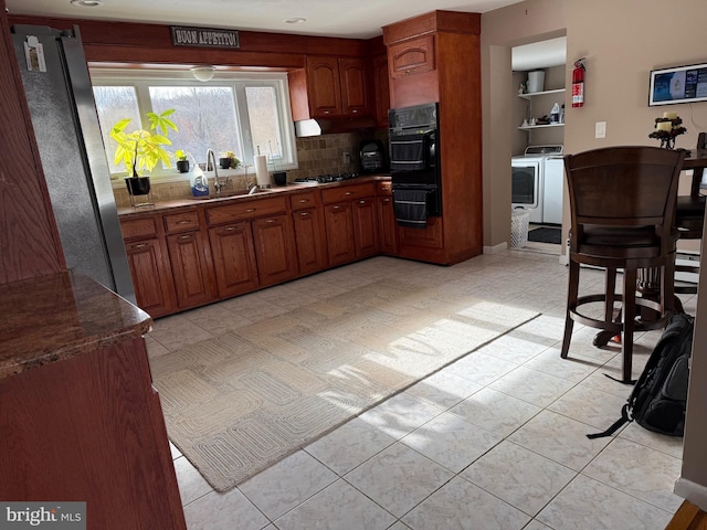 kitchen featuring appliances with stainless steel finishes, backsplash, washer and clothes dryer, sink, and light tile patterned flooring